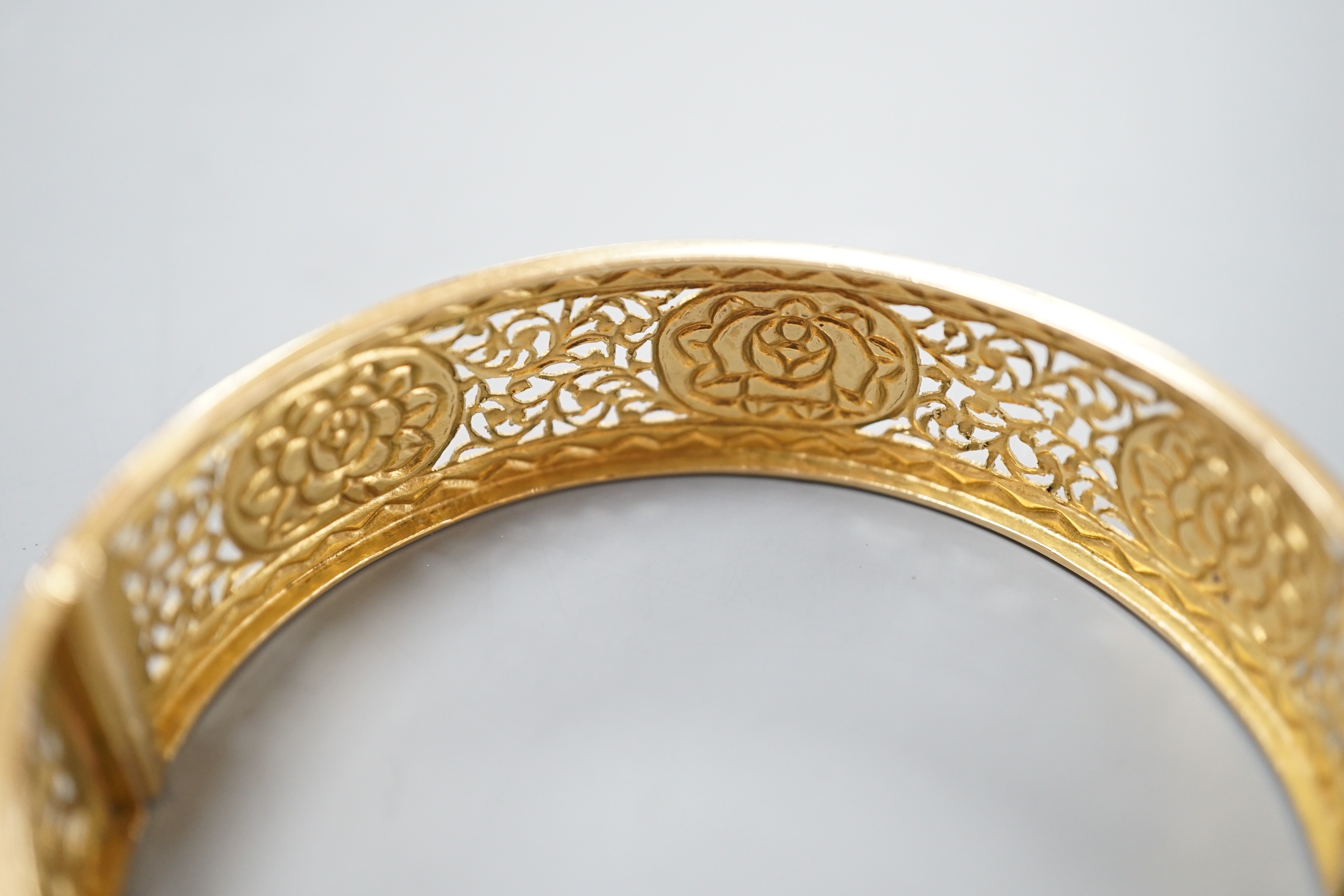 A pierced yellow metal and polychrome enamel set hinged bangle, gross weight 25.3 grams, (enamel a.f.).
